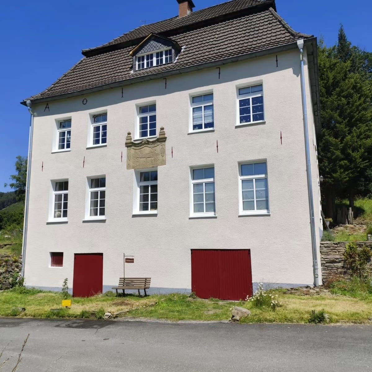 Historisches Wohnhaus mit frisch weiß gestrichener Fassade, roten Toren und Sandstein-Relief bei Sonnenlicht