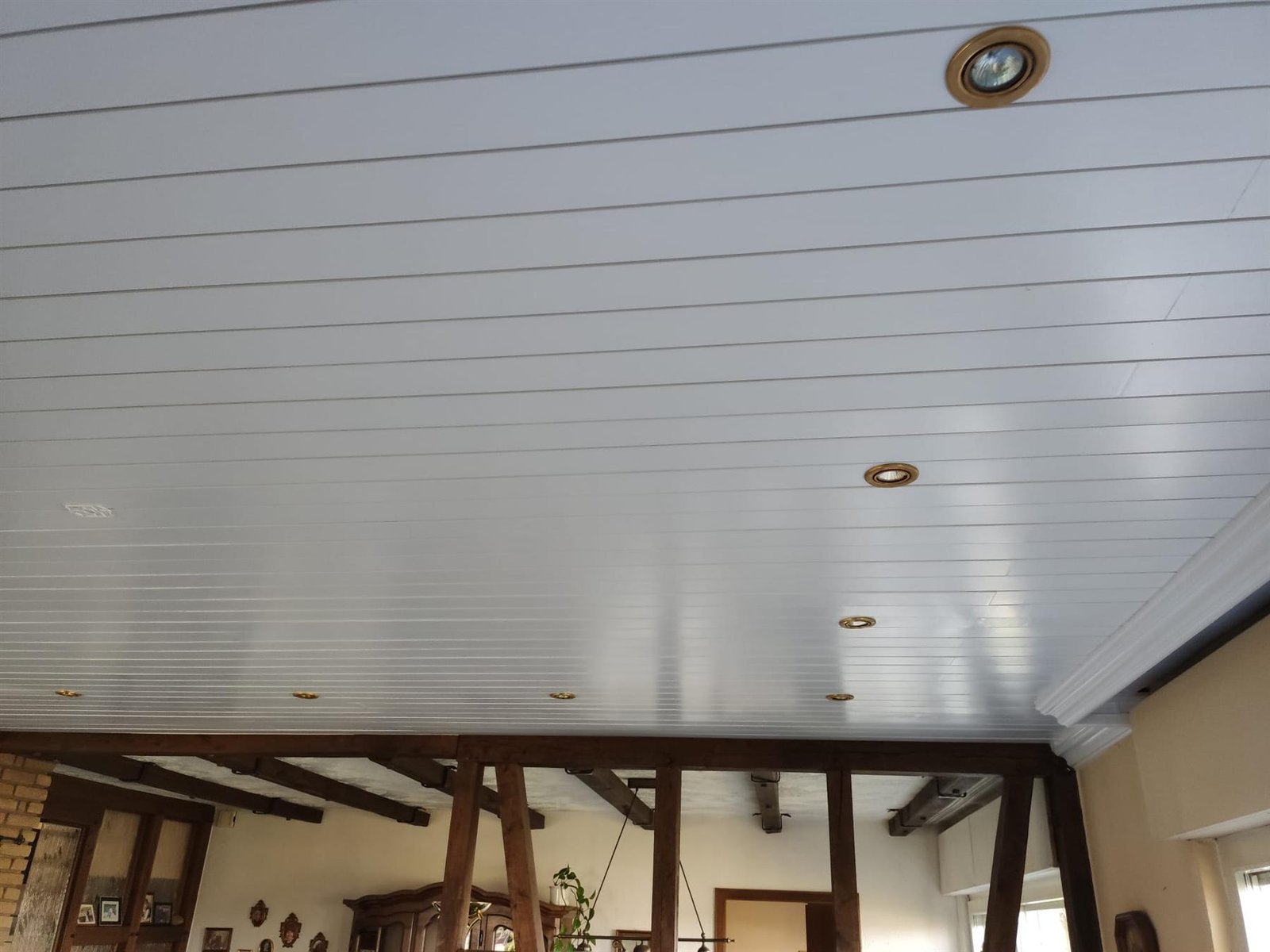 Frisch weiß lackierte Holzpaneeldecke mit Einbaustrahlern in einem Raum mit sichtbaren Holzbalken