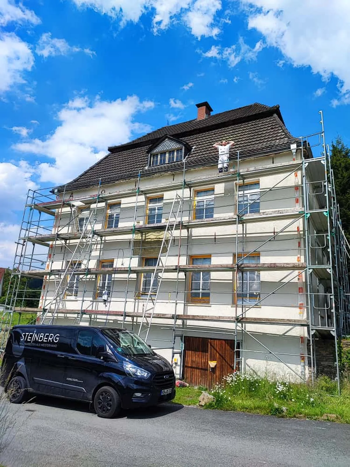 Handwerker bei Fassadenarbeiten am eingerüsteten Dachbereich eines Altbaus