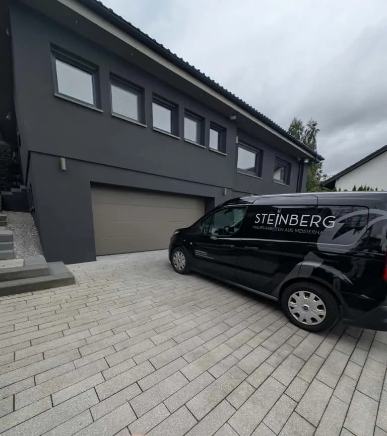 Moderner Neubau mit anthrazitfarbener Fassade und Firmenfahrzeug im Vordergrund