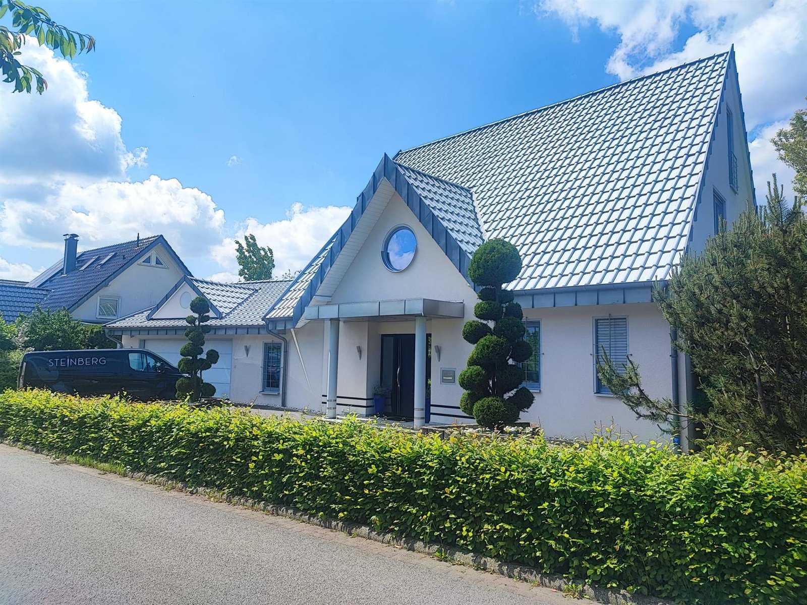 Weißes Wohnhaus mit dunklem Ziegeldach und gepflegtem Vorgarten