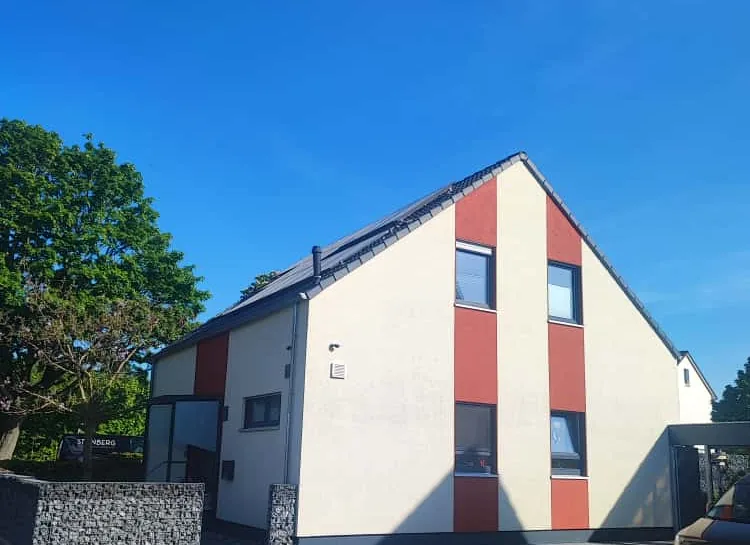 Verputzte Fassade mit rotem Farbakzent neben einer Gabionenwand