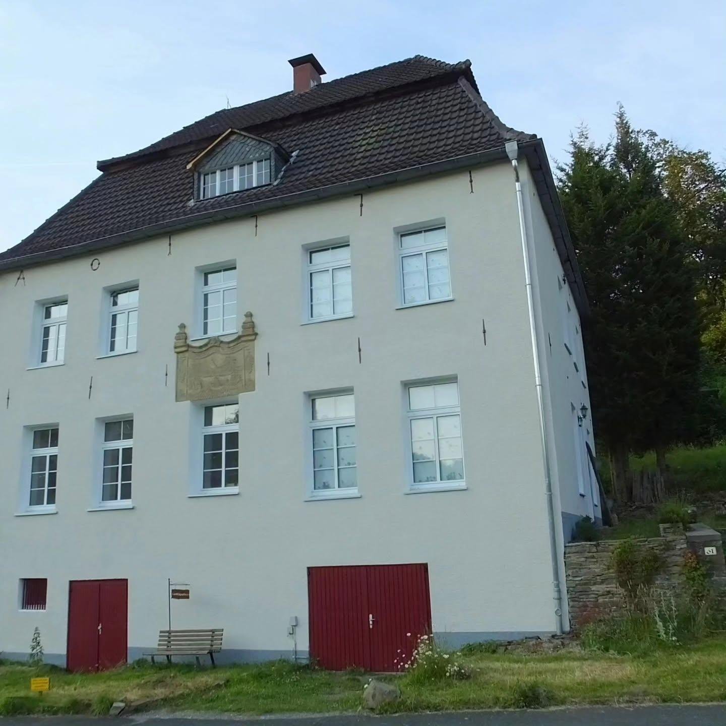 Dasselbe historische Putzgebäude mit Sandsteinrelief nach der Fassadenerneuerung, frisch hell gestrichen