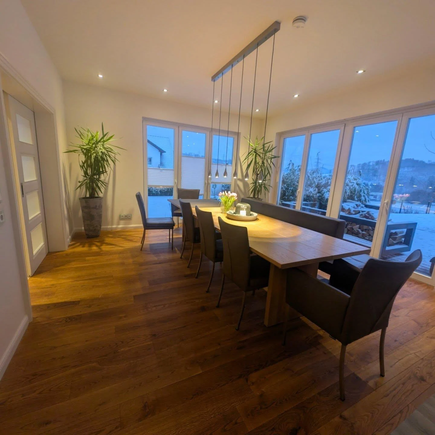 Esszimmer mit langem Holztisch, Pendelleuchten und Blick in den winterlichen Garten