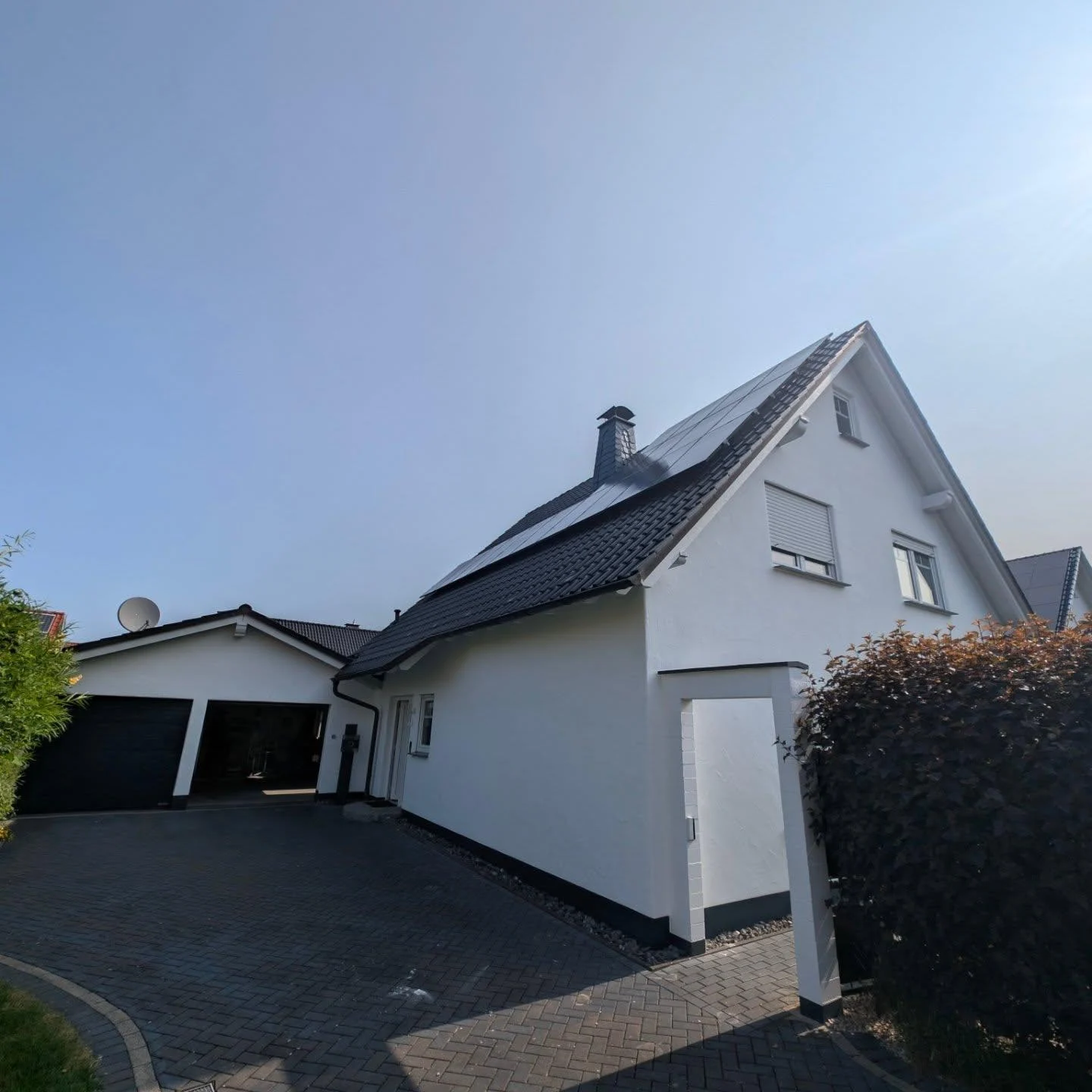 Weißes Einfamilienhaus mit dunklem Garagentor und gepflasterter Einfahrt in Ense