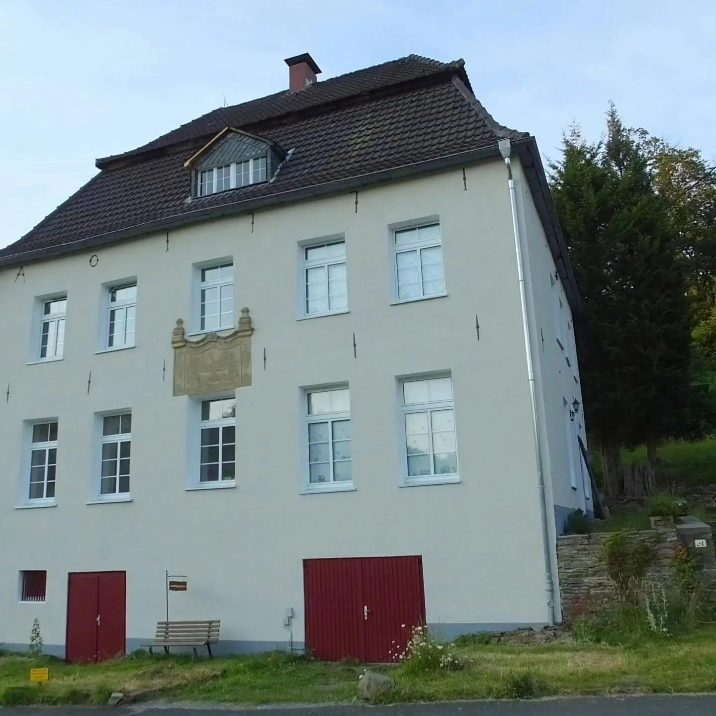 Dasselbe historische Putzgebäude mit Sandsteinrelief nach der Fassadenerneuerung, frisch hell gestrichen